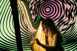 Eine Frau spielt vor einem Hintergrund mit bunten Kreisen auf einer Harfe
