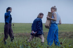 Drei Frauen stehen auf einem Acker, eine Frau trägt eine Holzkiste