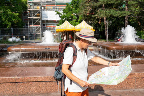 Ein Mann steht vor einem sprudelnden Brunnen und schaut in einen Stadtplan