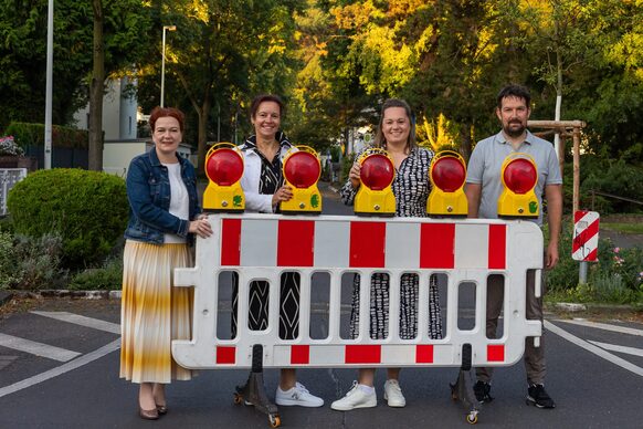 Vier Personen stehen hinter einer mobilen Absperrung vor einer temporären Schulstraße