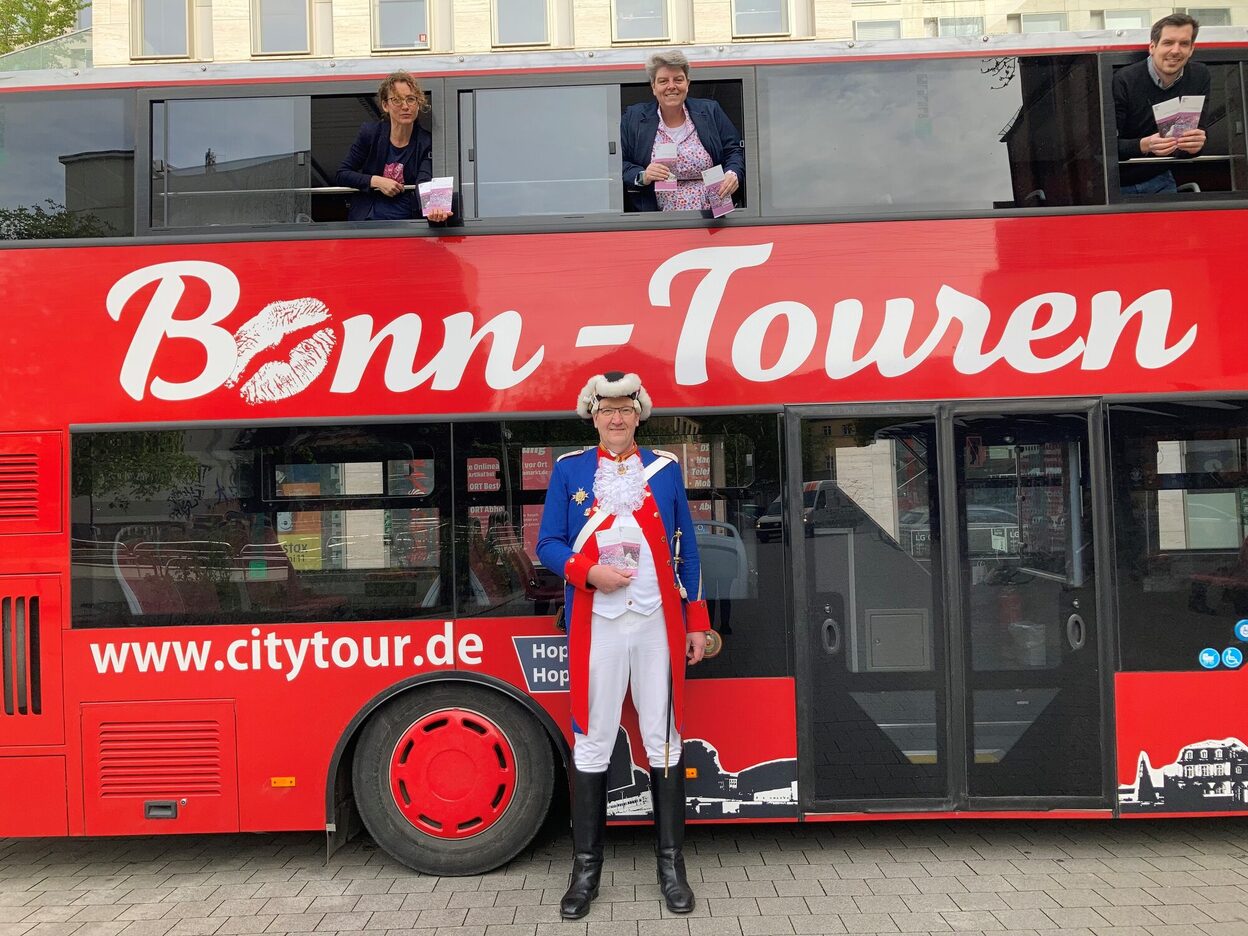 Das Team der Bonn-Information und ein Gästeführer stehen vor dem Stadtrundfahrt-Bus.