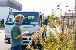 Frau mit Tablet an einem Baumbeet, im Hintergrund ein Wasserwagen.