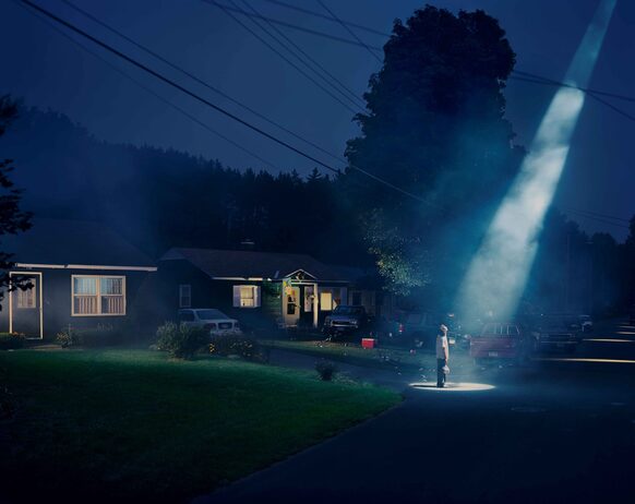 In der Nacht steht ein Mann vor seinem Haus in einem Lichtstrahl von oben