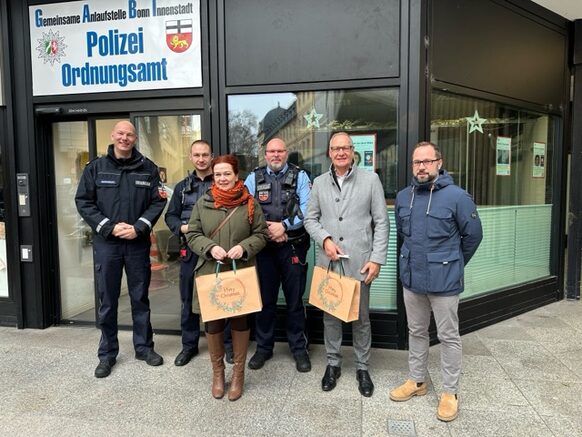 Sechs Personen stehen vor dem Eingang eines Gebäudes, das eine große Tafel über der Tür als "Gemeinsame Anlaufstelle Bonn Innenstadt" von Polizei und Ordnungsamt ausweist.