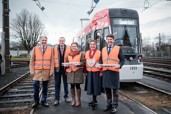 Fünf Personen in orangefarbenen Warnwesten stehen vor einer neuen Straßenbahn