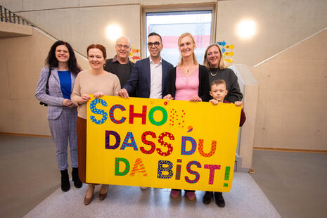 Gruppenbild mit den Gästen, die vor sich ein großes Schild halten, auf dem in bunten Buchstaben steht "Schön, dass Du da bist!"