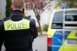 Polizist im Vordergrund telefoniert. Im Hintergrund steht ein Polizeiauto.