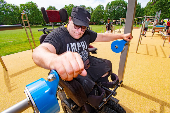 Mann im Rollstuhl an einem Outdoor-Fitnessgerät.