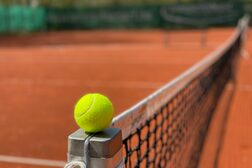 Ein gelber Filztennisball liegt auf dem Pfosten des Tennisnetzes