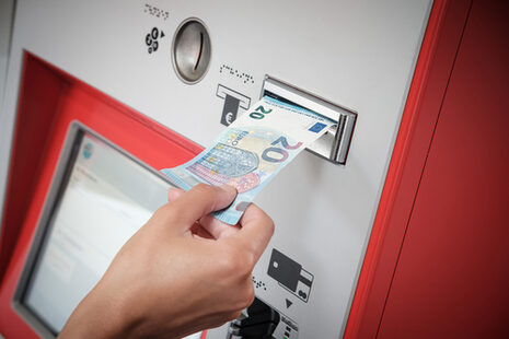 Eine Person schiebt einen 20-Euro-Schein in einen Ticketautomaten