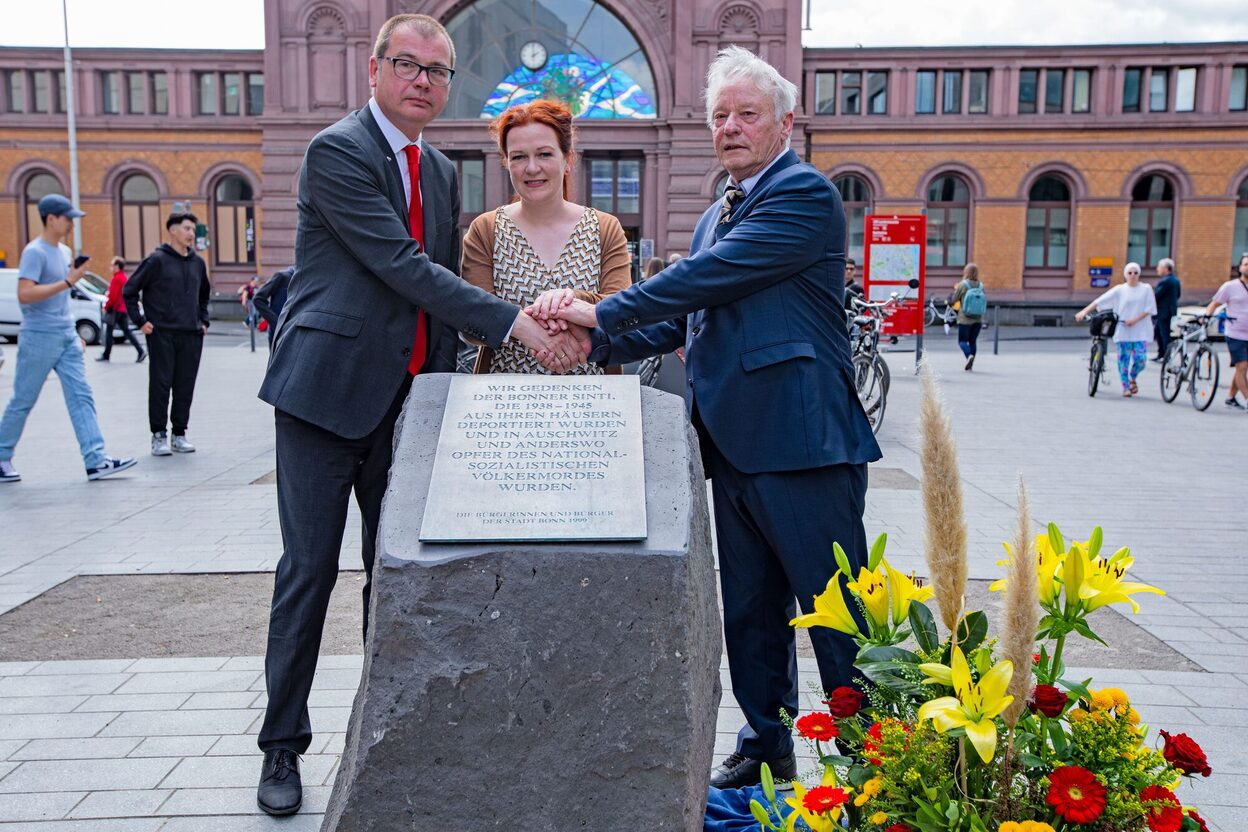 Das Bild zeigt die Enthüllung der Gedenktafel für Sinti und Roma, die auf einem Findling vor dem Bonner Hauptbahnhof wieder angebracht wurde.