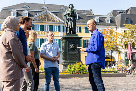 Das Bild zeigt einen Gästeführer mit einer Gruppe am Beethoven-Denkmal auf dem Münsterplatz.