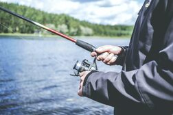 Ein Angler steht mit einer Angel in der Hand an einem Gewässer