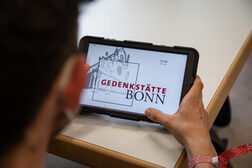 Eine Person betrachtet das Logo der Gedenkstätte Bonn auf einem Smartphone