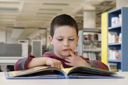 Ein Junge liest in einem Buch und legt nachdenklich den Finger an die Lippen