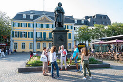 Das Bild zeigt einen Gästeführer mit einer Gruppe am Beethoven-Denkmal auf dem Münsterplatz.