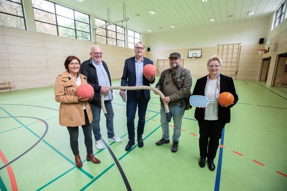 Gruppenbild mit fünf Personen, die Sportutensilien in den Händen halten, in der neuen Sporthalle.