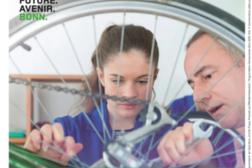 Auf dem Plakat ist ein Foto von einer Frau und einem Mann zu sehen, die an einer Fahrradspeiche schrauben. Darüber ist zu lesen „Bonner Klimapreis“.