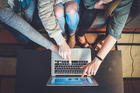 Drei Personen sitzen gemeinsam vor einem Laptop und deuten auf den Monitor