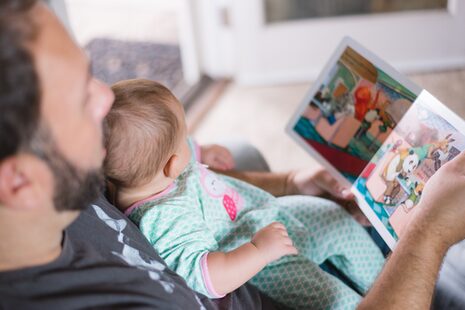 Ein Vater schaut mit einem Kleinkind ein Bilderbuch an