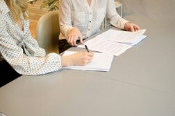 Zwei Frauen sitzen an einem Tisch, auf dem Blätter liegen.