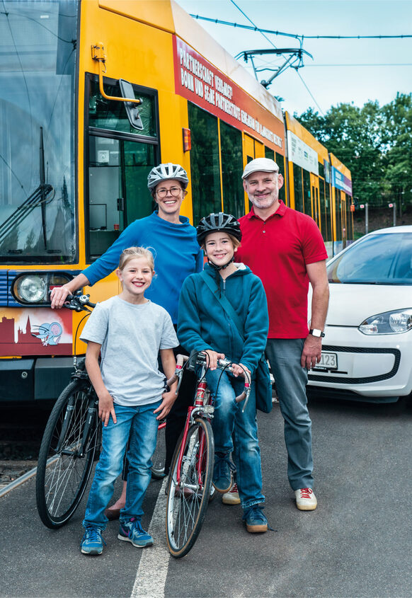 Familie mit Fahrrädern steht vor einem Bus und einem Pkw.