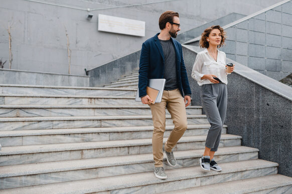 Ein Mann mit einem Laptop unter dem Arm und eine Frau gehen eine Außentreppe hinunter
