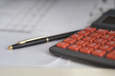 Taschenrechner mit roter Tastatur, Papier und ein Stift