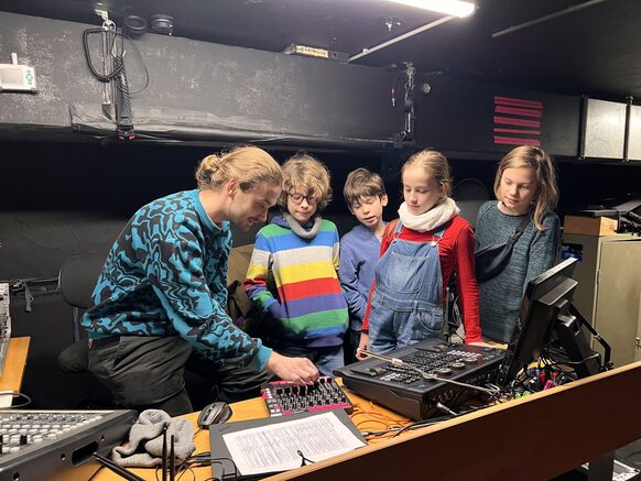 Vier Kinder schauen einem Bühnentechniker bei der Arbeit zu