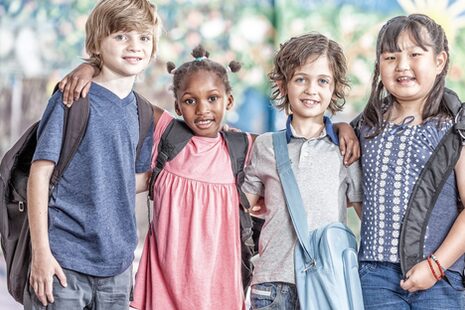 Schulkinder aus verschiedenen Ethnien und Kulturen halten sich freundschaftlich im Arm