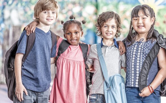 Schulkinder aus verschiedenen Ethnien und Kulturen halten sich freundschaftlich im Arm