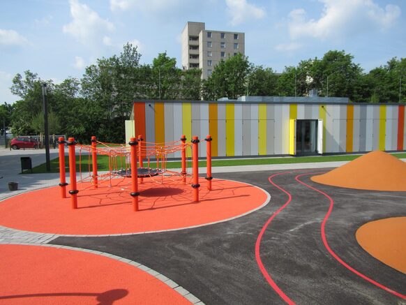 Das Gebäude des Quartiers- und Jugendzentrum Auerberg. Im Vordergrund der Spielplatz mit Klettergerüst.