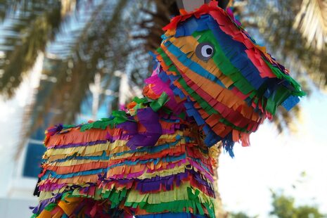 In einer Palme hängt eine Pinata in bunten Regenbogenfarben