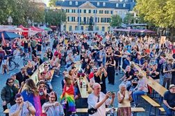 Blick von der Beethovens-Bunte-Bühne auf den Münsterplatz und das Postamt im Hintergrund. Hunderte Menschen, die teilweise queere Flaggen um die Schultern gebunden haben, schauen auf die Bühne, tanzen, jubeln und machen Fotos.