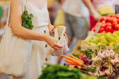 Eine Frau kauft an einem Marktstand Möhren und Knoblauch