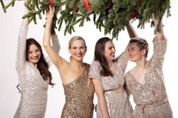 Vier Frauen in glitzernden Kleidern halten einen Tannenbaum hoch